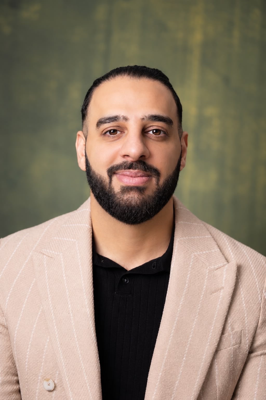 Portrait of Taher Adel in a beige pinstripe jacket against a green backdrop